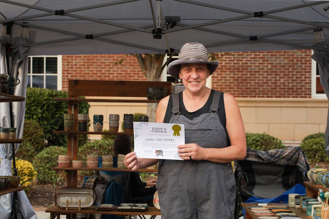 Award-winning vendor holding her certificate at her booth